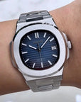 Silver watch with a blue face on a wrist against a neutral background