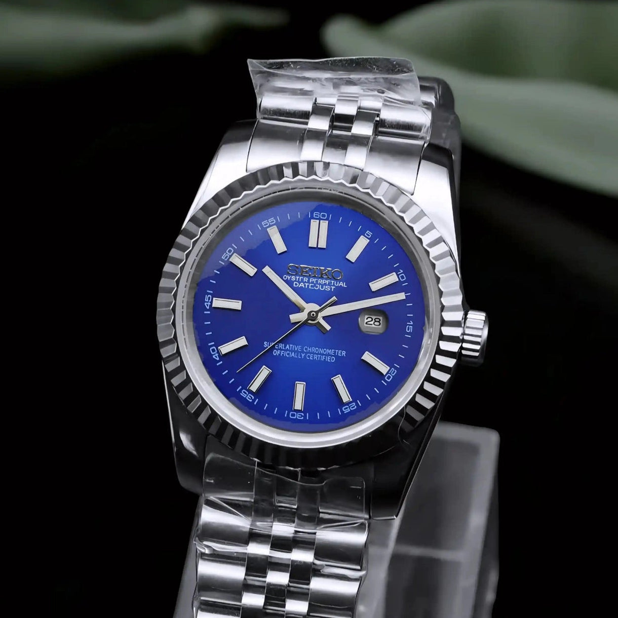 Silver watch with blue face on a clear stand against a dark background