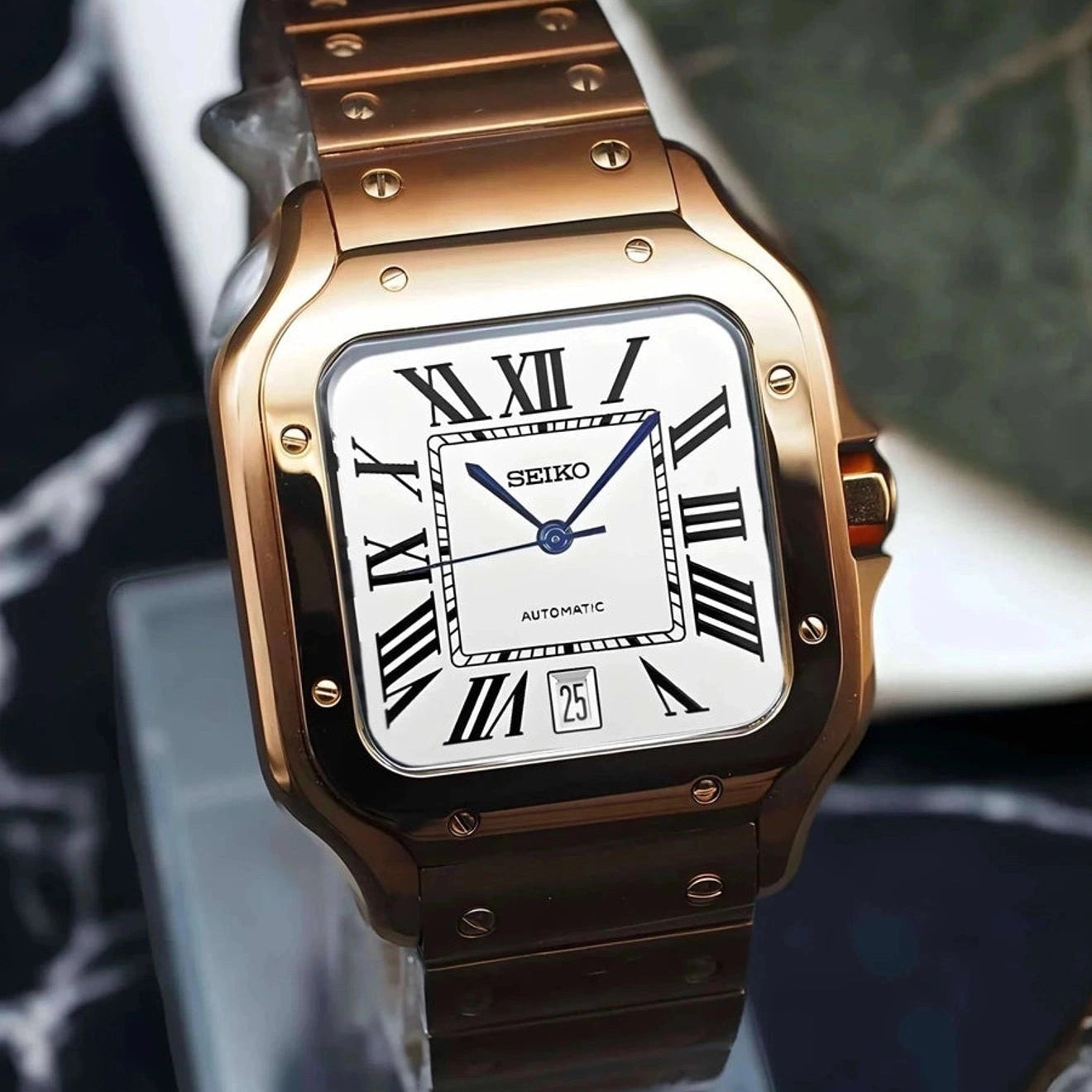 Rose gold Seiko watch with white face and black Roman numerals on a reflective surface.