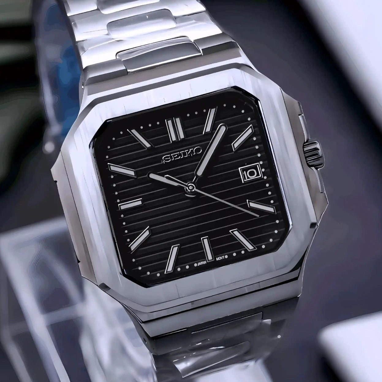 Silver watch with black face on a reflective surface