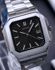 Silver watch with black face on a reflective surface