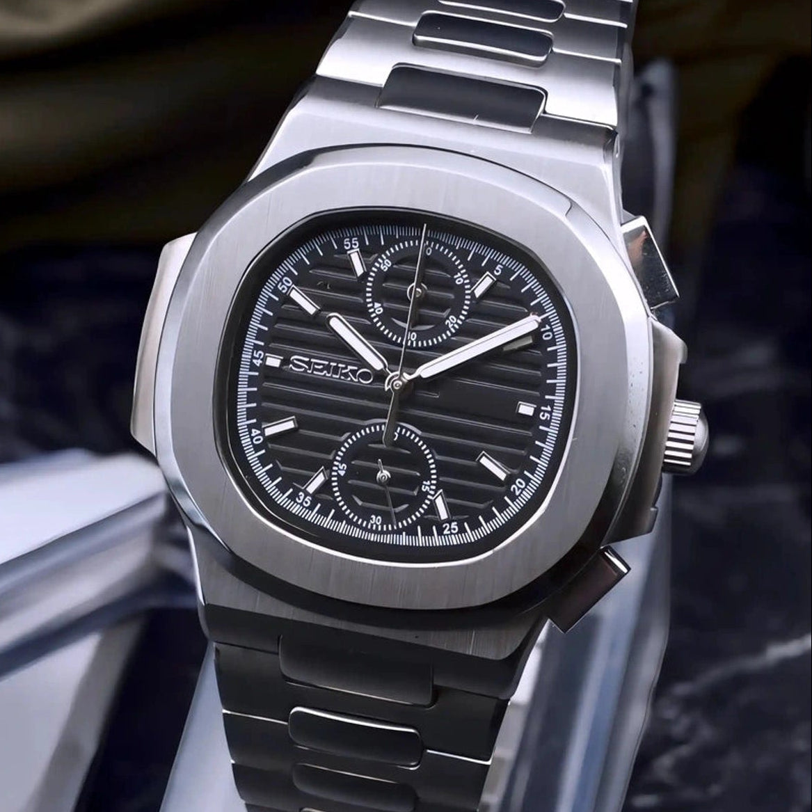 Silver watch with black chronograph dial on a black marble stand 