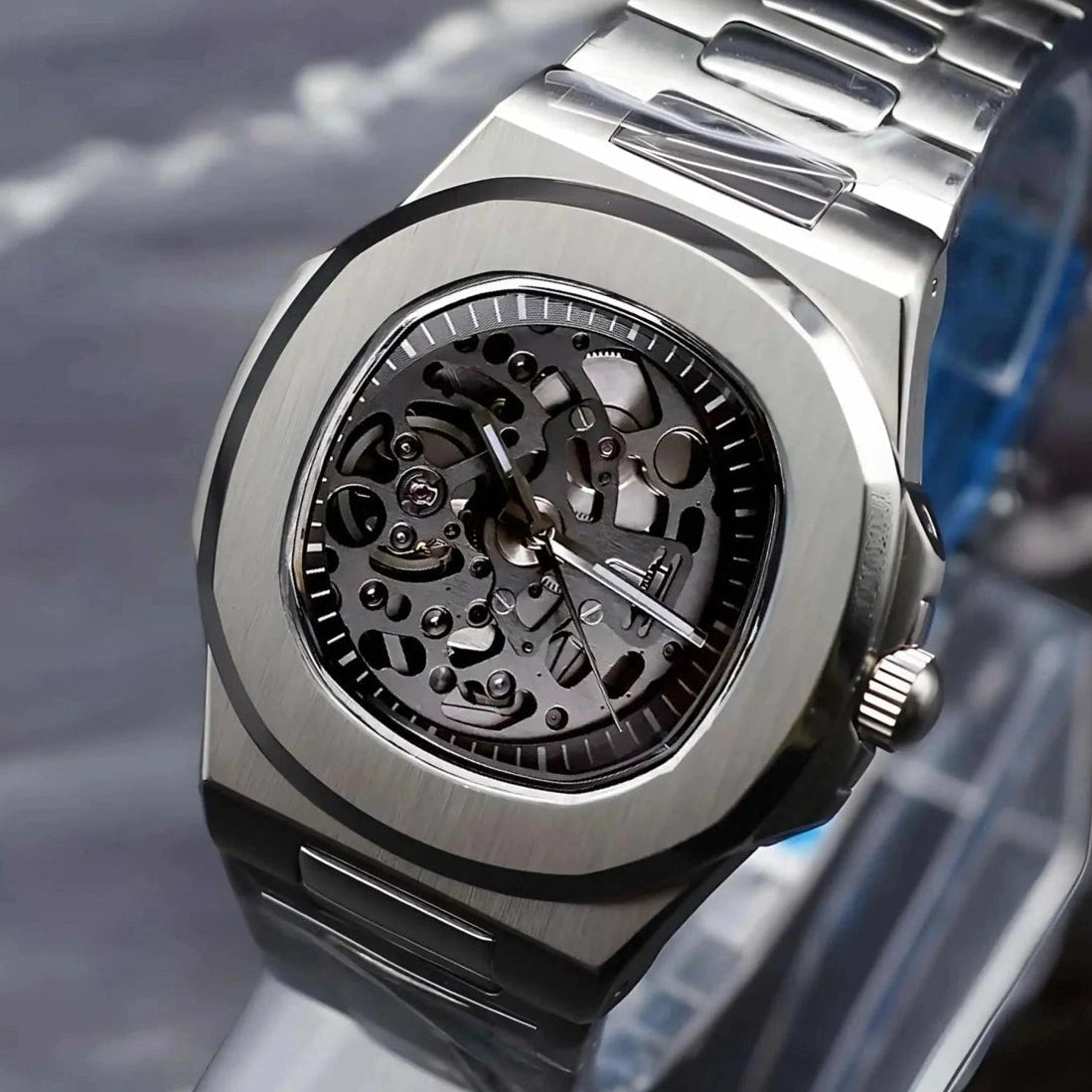 Silver skeleton watch on a clear stand with a dark marble background