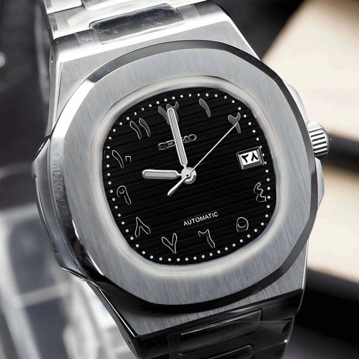 Silver and black watch with arabic hour indicies on a stand