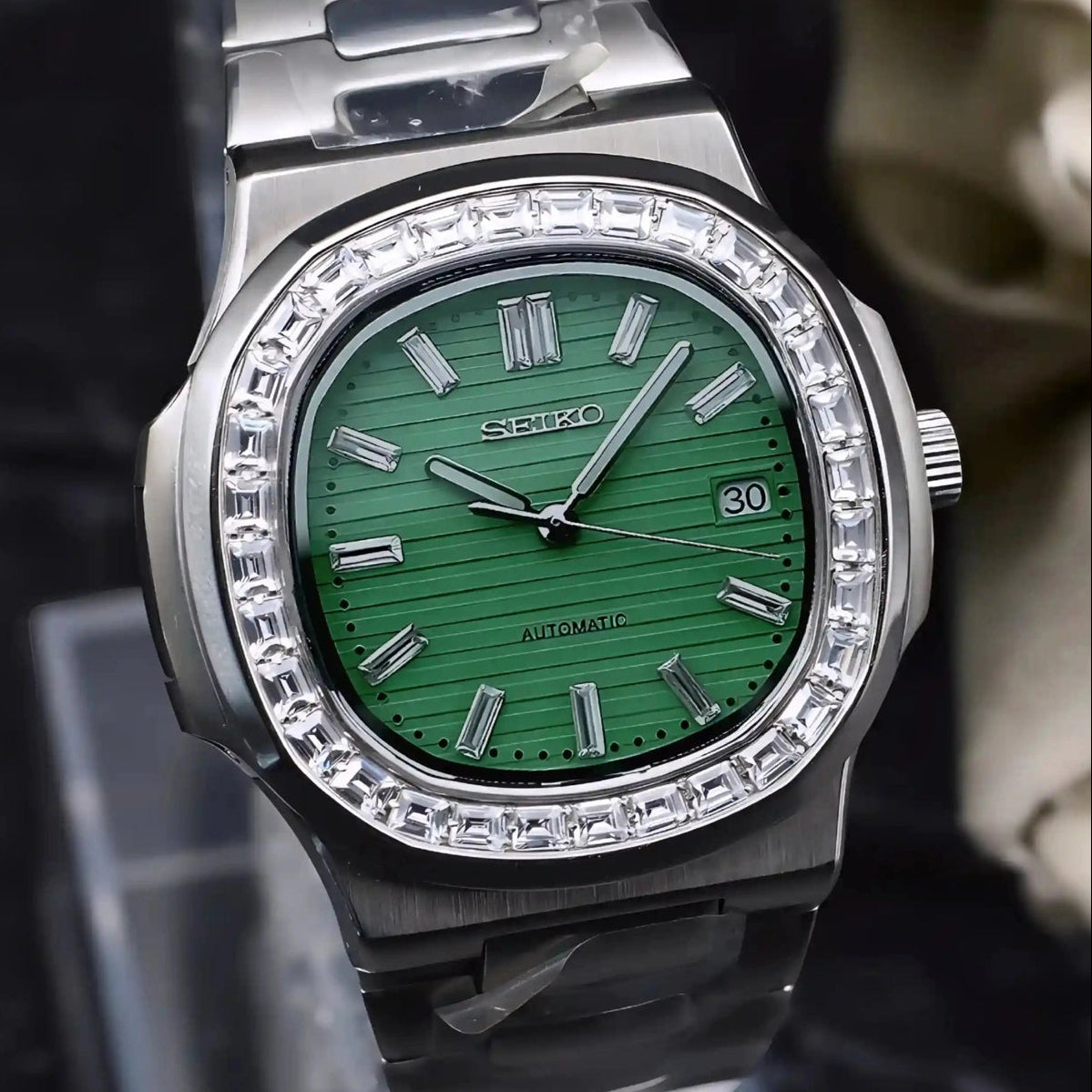 Silver watch with green face on a stand.