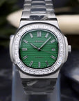 Silver watch with green face on a clear stand against a dark background