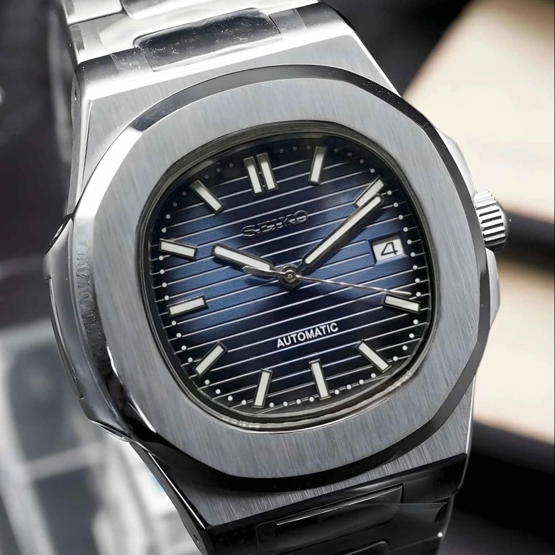 Silver watch with blue face on a reflective surface