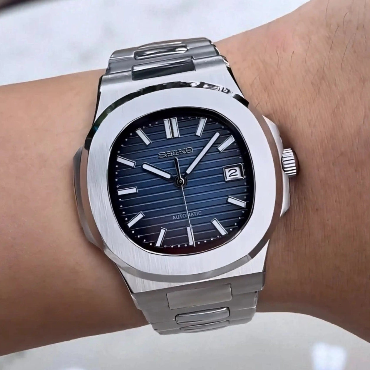 Silver watch with a blue face on a wrist against a neutral background